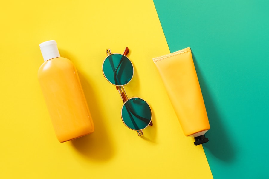 Summer Bright Flatlay On Colorful Background With Tubes And Bottle With Sunscreen, Green Sunglasses.