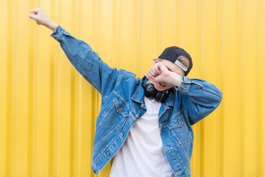 Young Man Wearing Layered Clothes Throws Dab On The Background Of A Yellow Wall.