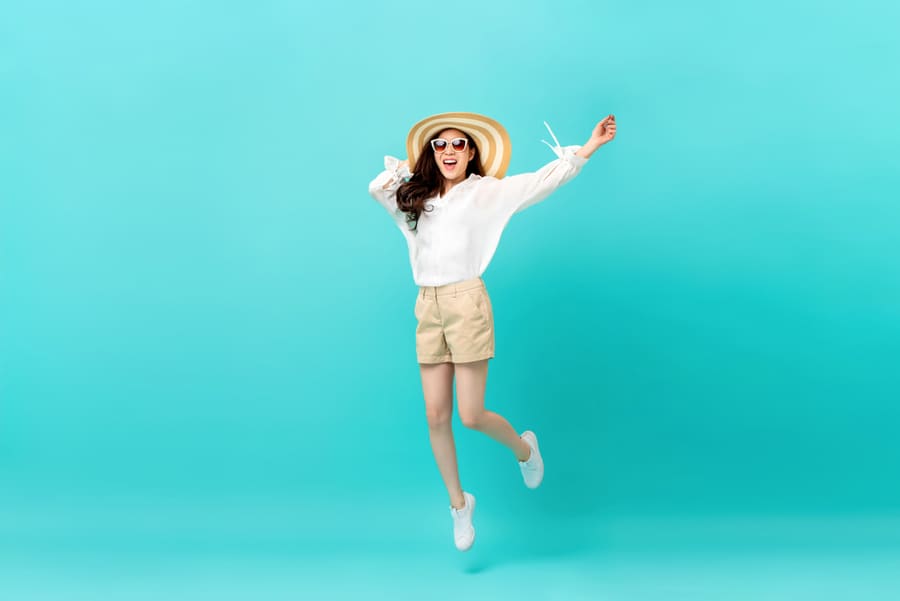 Studio Shot Of Happy Energetic Asian Woman Wearing Summer Fashion Attire Jumping In Mid-Air Motion Isolated In Light Blue Background