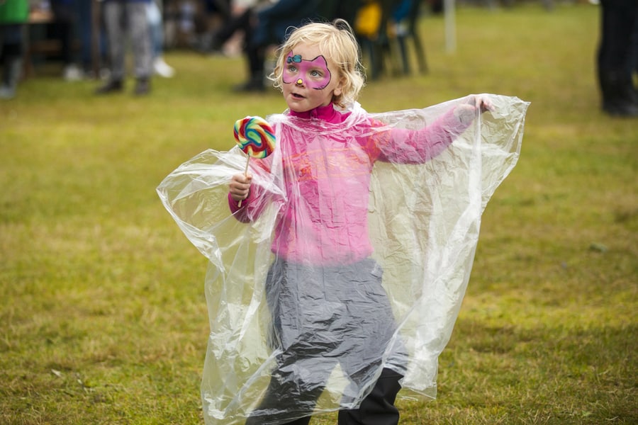 Little Girl With Make Up On Her Face Having A Rainbow Lollipop And Wearing A Rain Poncho