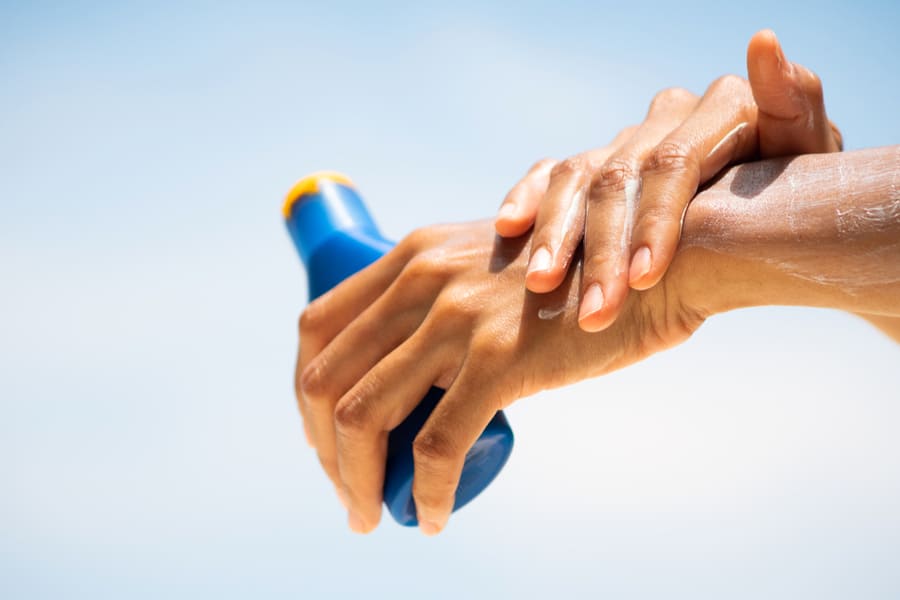 Woman Applying Sunscreen On Her Hands From A Bottle