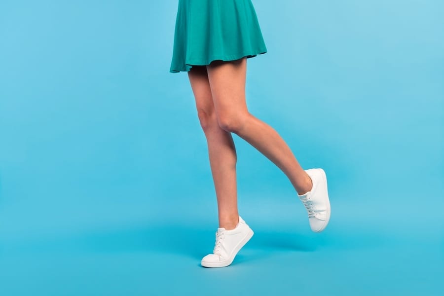 Cropped Photo Of Pretty Charming Young Lady Legs Wear Green Mini Skirt Sneakers Isolated Blue Color Background