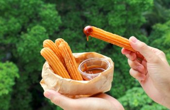 Hand Dipping A Stick Of Fresh Fried Churro In Dolce De Leche Or Caramel Sauce