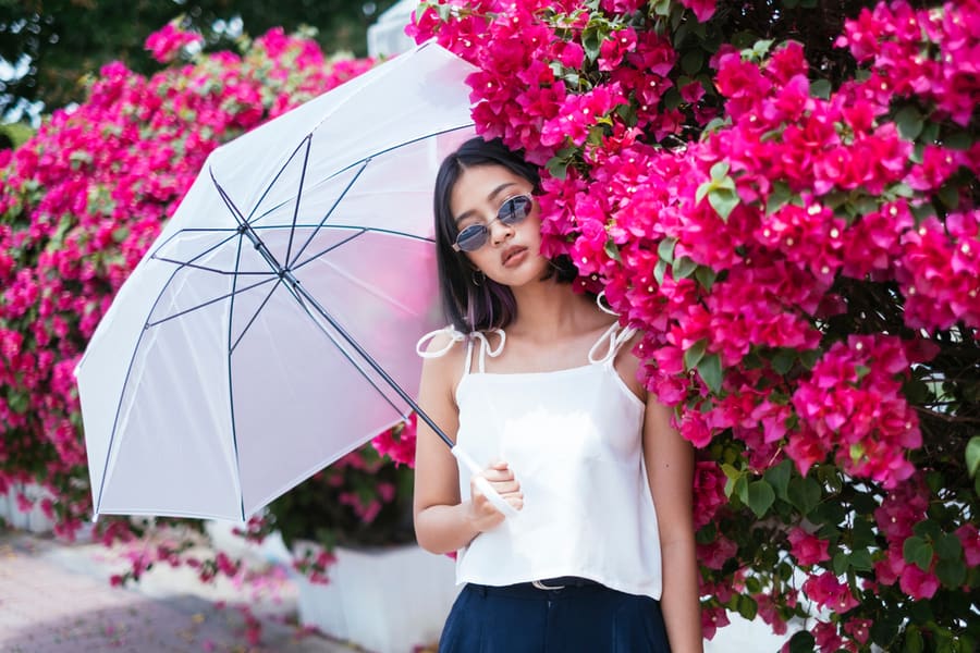 Portrait Of Asian Woman Wearing Sunglasses, Holding White Umbrella, With Pink Flower On Background.