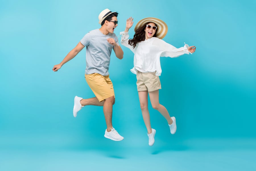 Smiling Energetic Asian Couple Tourists In Summer Casual Clothes Jumping Isolated On Light Blue Studio Background