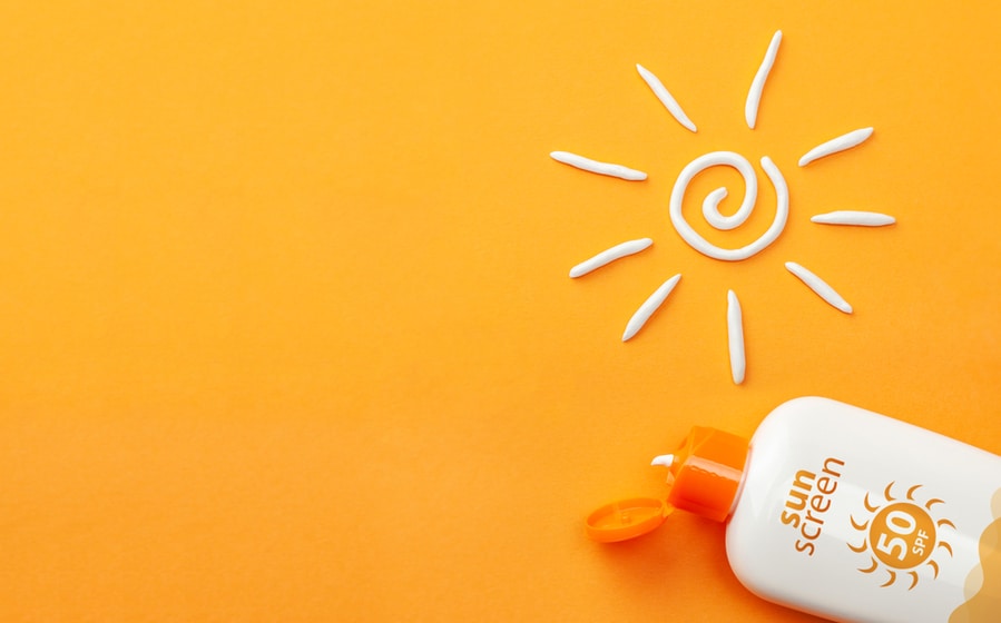 Sunscreen On Orange Background. Plastic Bottle Of Sun Protection And White Sun-Shaped Cream.