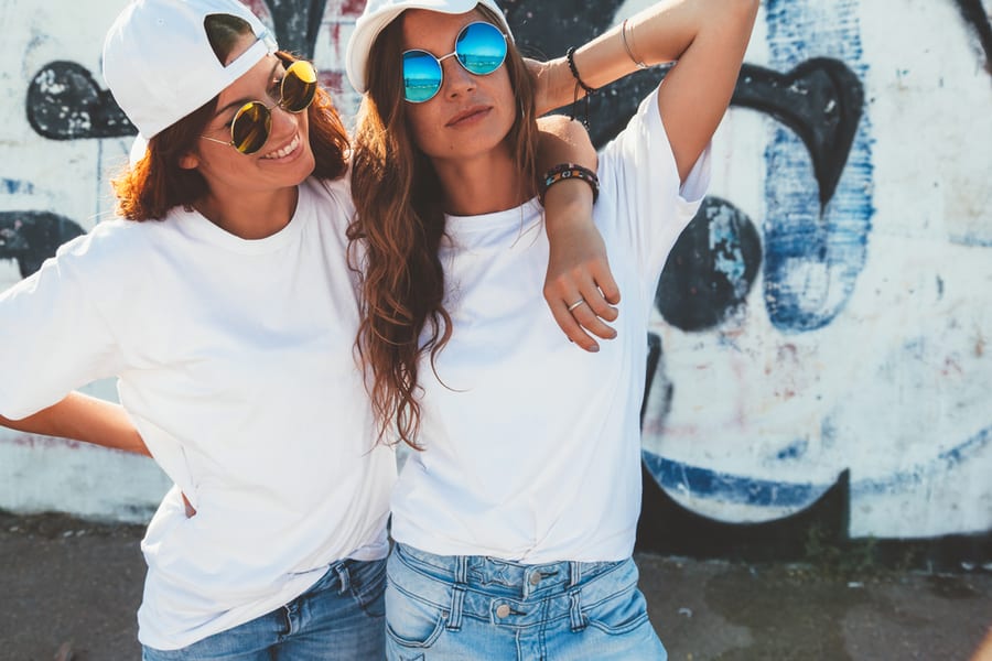 Two Models Wearing Plain White T-Shirts And Hipster Sunglasses Posing Against Street Wall