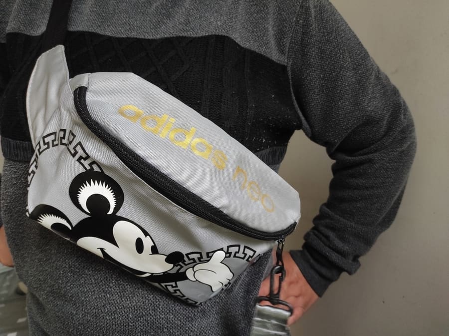 A Person In A Black Sweater Wearing An Adidas Waist Bag With Mickey Mouse Print