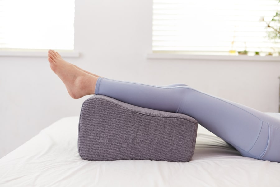 A Woman In Leggings Lying In Bed Resting With A Cushion On Her Feet