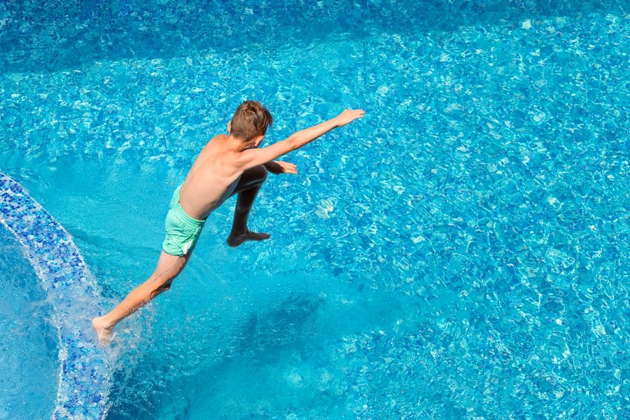 Child Boy Jumping Into Blue Water Of Hotel Swimming Pool