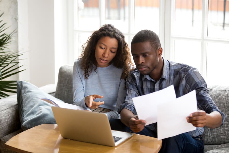 Couple Discussing Paper Documents, Sitting Together On Couch At Home
