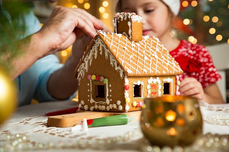 Father And Adorable Daughter In Red Hat Building Gingerbread House Together