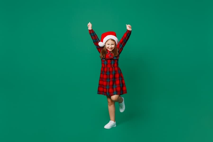 Full Body Fun Merry Little Child Kid Girl 7 Years Old Wear Red Dress Christmas Hat Posing Do Winner Gesture Celebrate Clench Fists Isolated On Plain Dark Green Background.