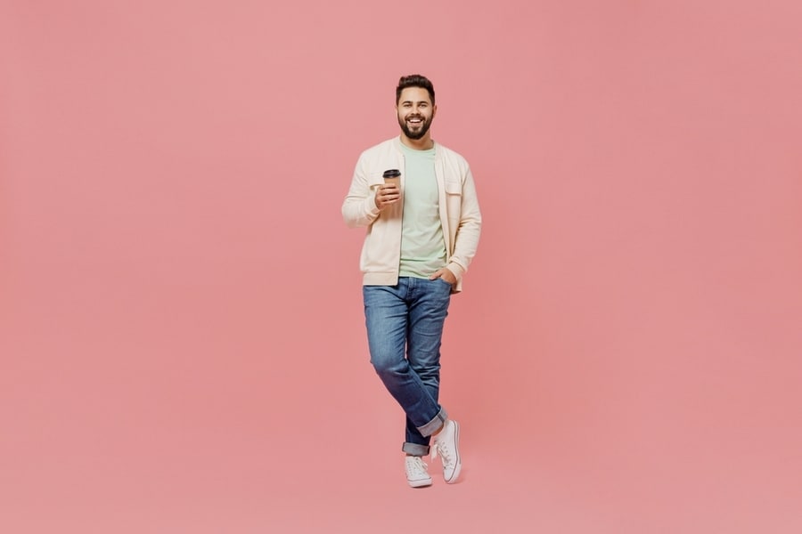 Full Body Young Smiling Happy Man 20S In Trendy Jacket Shirt Hold Takeaway Delivery Craft Paper Brown Cup Coffee To Go Isolated On Plain Pastel Light Pink Background Studio.