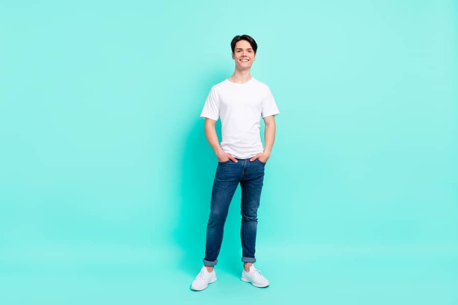Full Length Photo Of Nice Brunet Hairdo Teen Guy Stand Wear T-Shirt Jeans Isolated On Teal Color Background