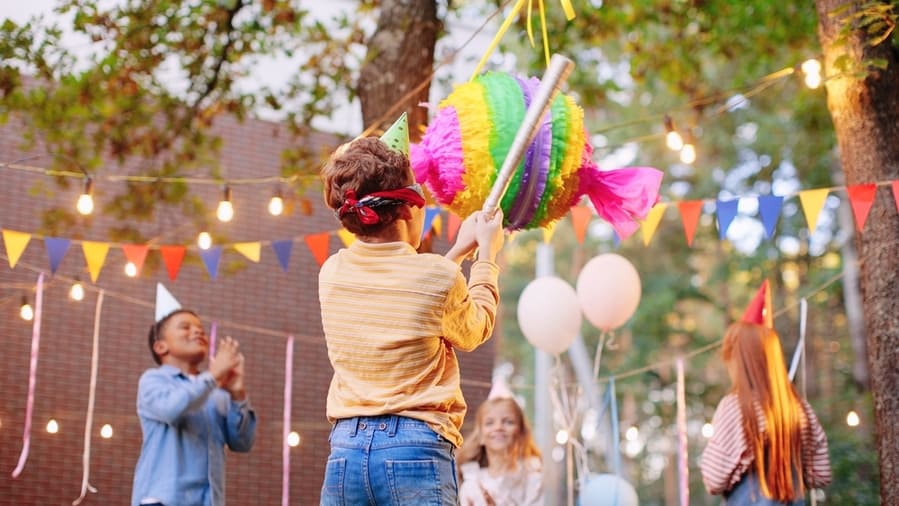 Group Of Children Smash Pinata With A Bat At Birthday Party