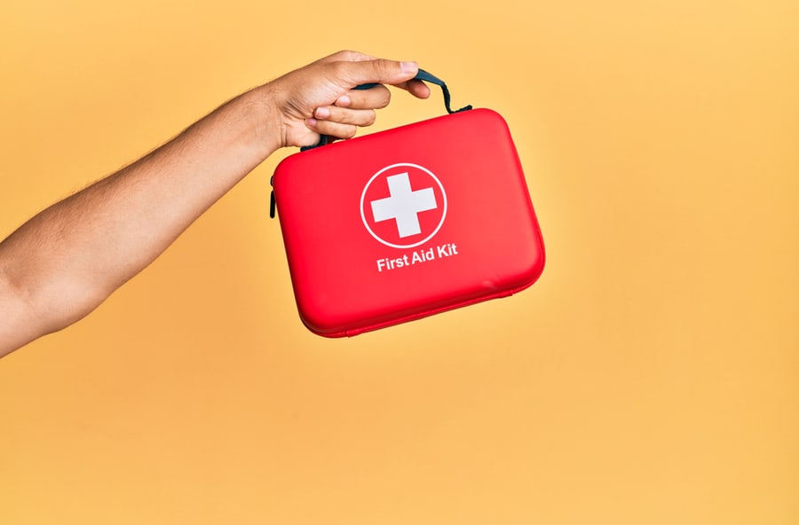 Hand Of Hispanic Man Holding First Aid Kit Over Isolated Yellow Background.