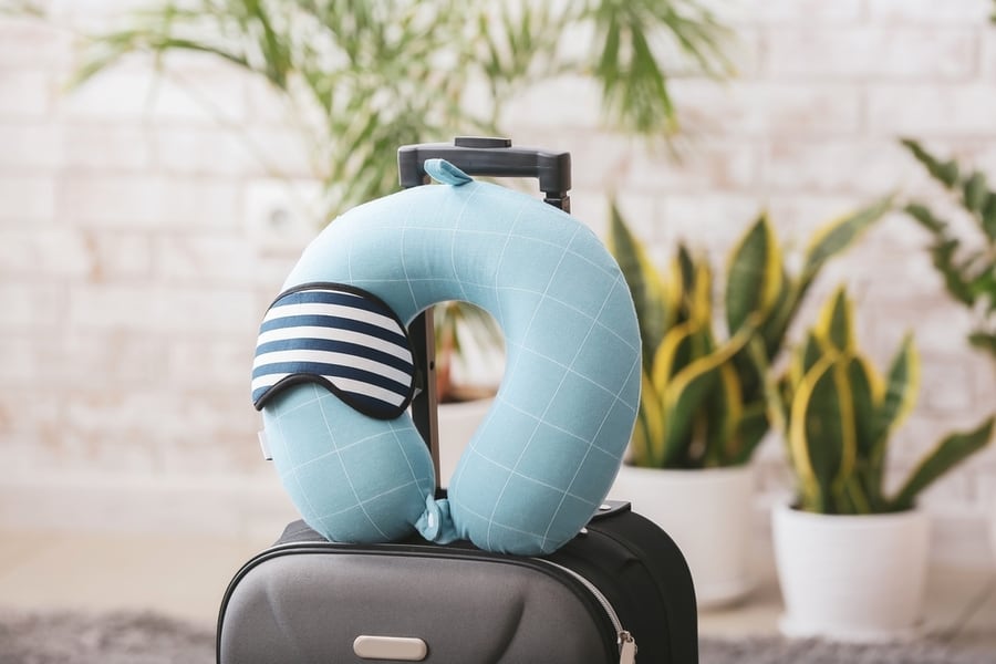 Travel Pillow, Sleep Mask And Suitcase On Floor In Room