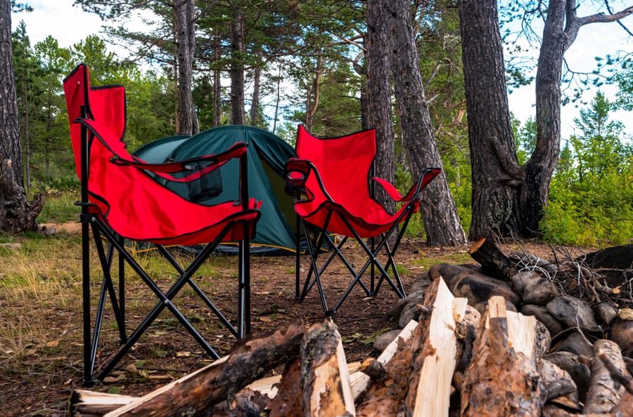 View Of Tourist Camp With Red Folding Chairs, Camping Tent And Firewood Near The Bonfire In The Forest