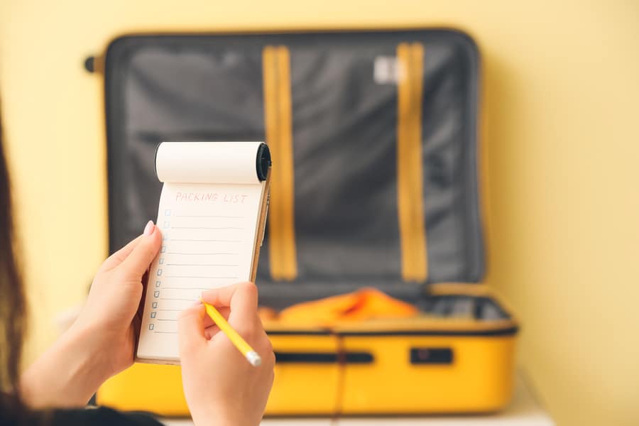Woman Making Check-List Of Things To Pack For Travel At Home