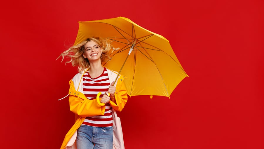 Young Happy Emotional Cheerful Girl Laughing And Jumping With Yellow Umbrella On Colored Red Background